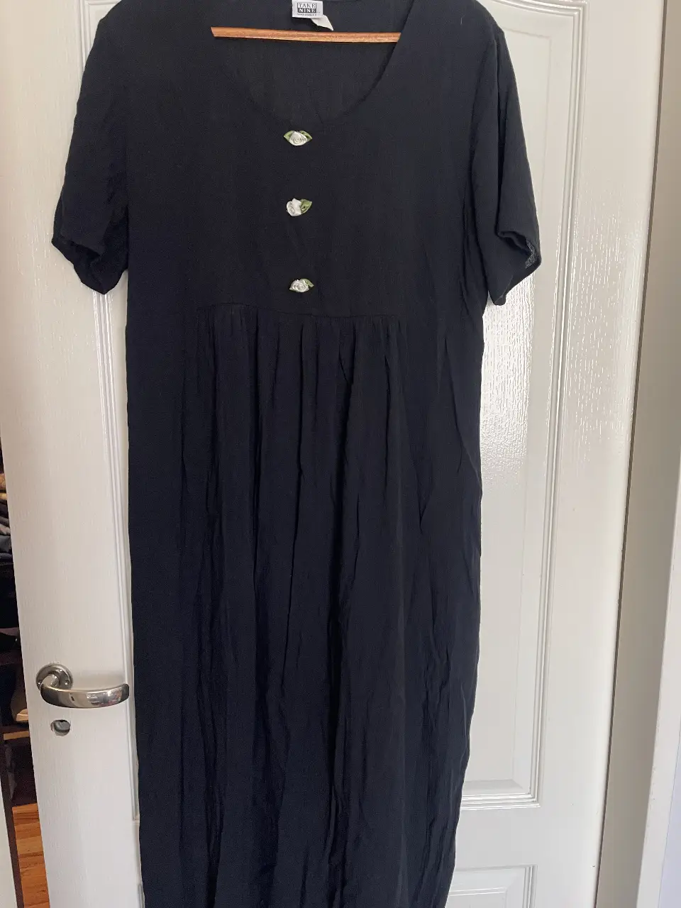 Vestido midi negro con botones decorativos en la parte delantera. Corte holgado y mangas cortas. Ideal para un look casual y cómodo.