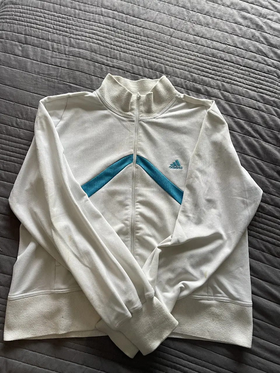 Buzo deportivo Adidas blanco con detalles en azul. Con cierre frontal y cuello alto. Talle XL.