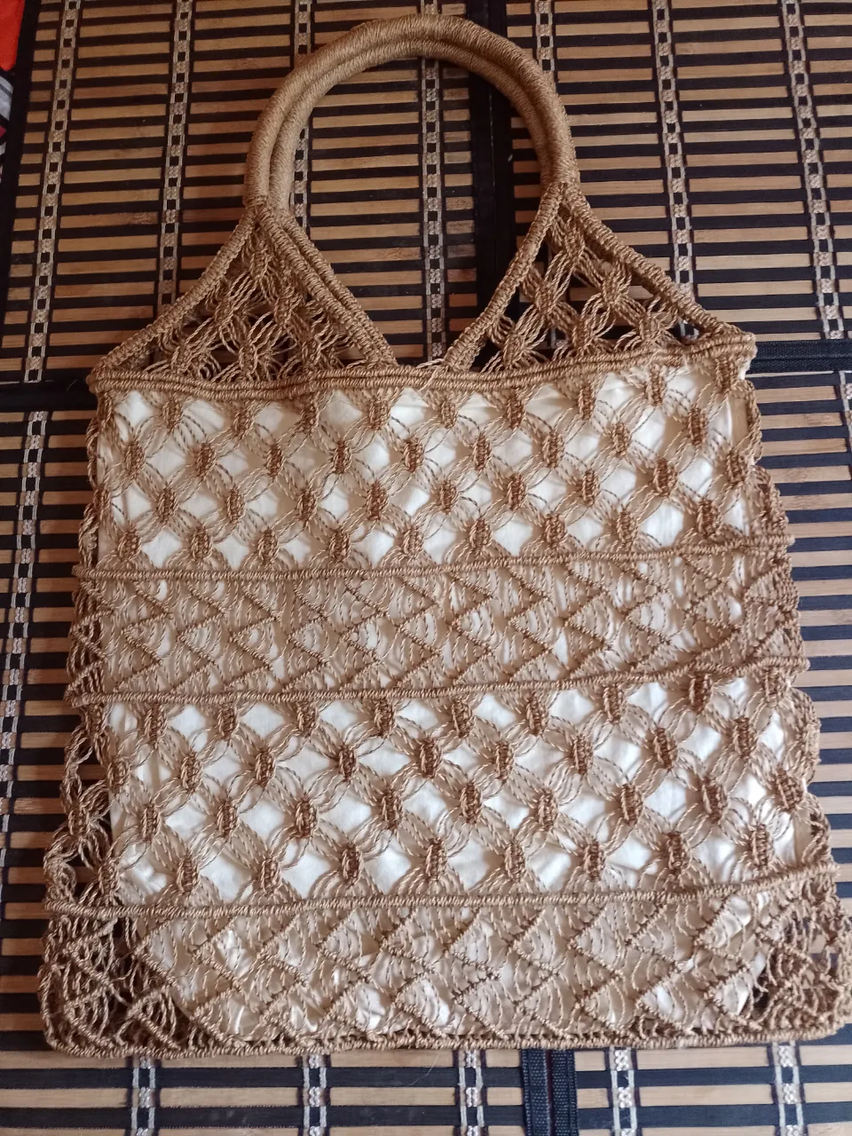 Bolso de mano tejido color marrón con forro blanco. Posee dos manijas.