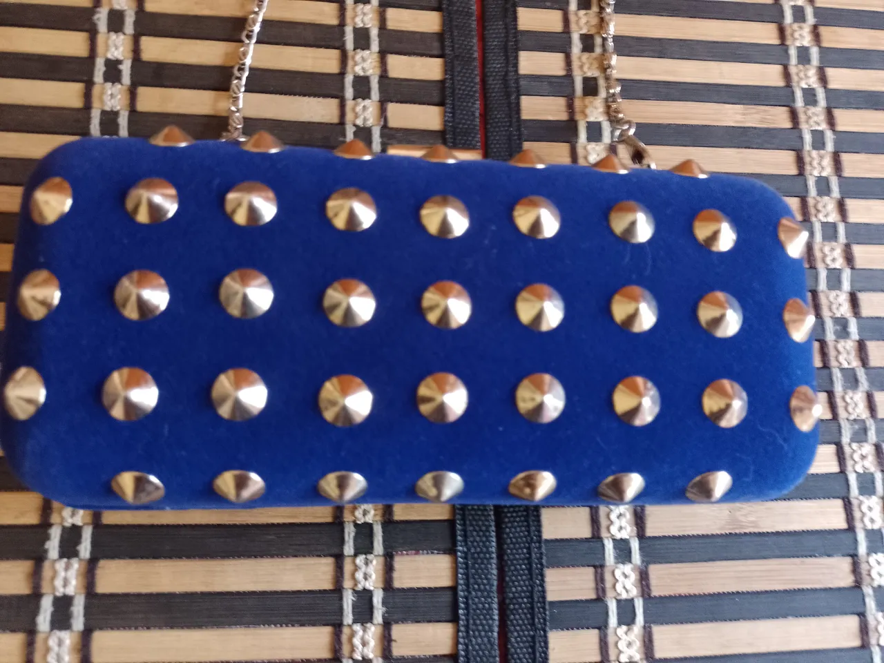 Cartera azul de terciopelo con tachas doradas y cadena metálica.