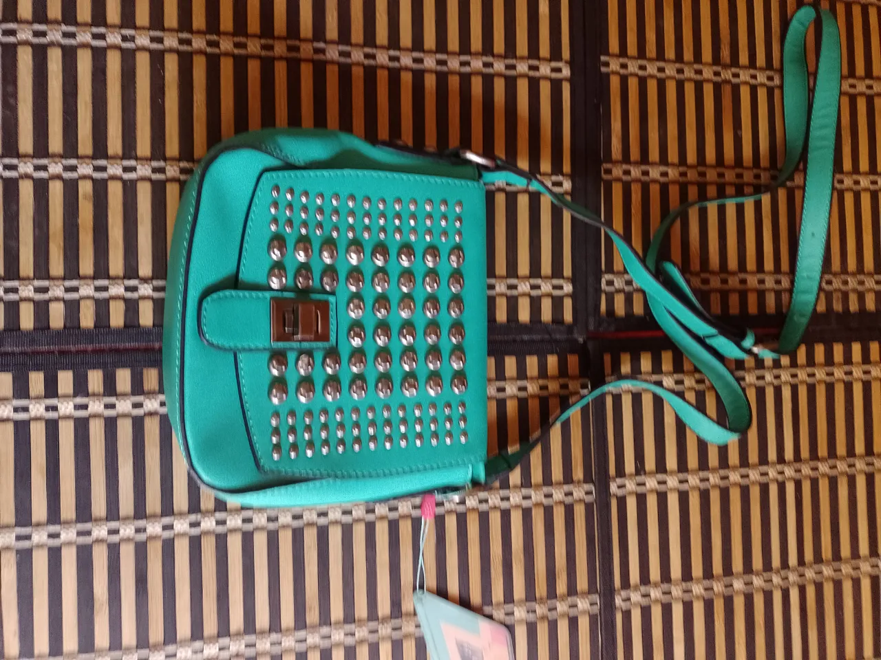 Cartera de color verde con tachas plateadas en el frente. Posee una correa larga para colgar.