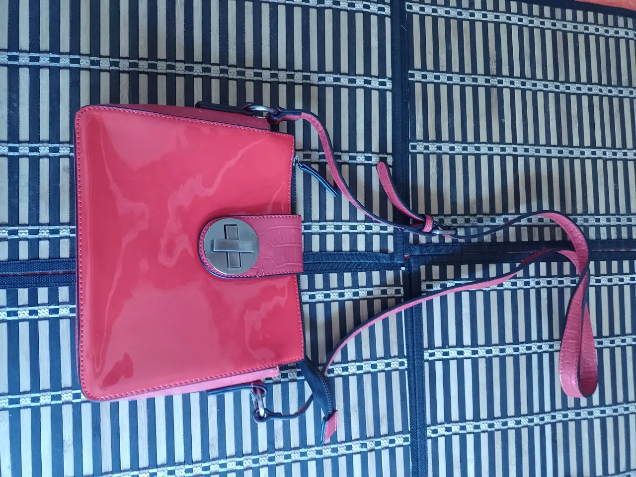 Cartera de charol color rojo con detalles en cocodrilo y cierre.