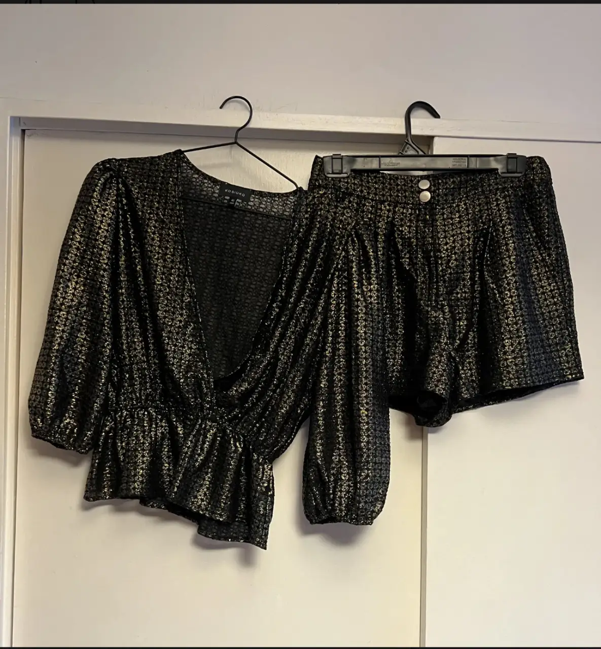 Conjunto de dos piezas negro con detalles dorados. Incluye una blusa con mangas abullonadas y un short a juego. Ideal para fiestas y eventos especiales.