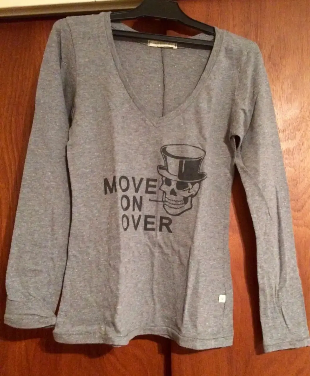 Remera manga larga gris con cuello en V y estampado de calavera con sombrero y la frase 'MOVE ON OVER'. Ideal para un look casual y con onda.