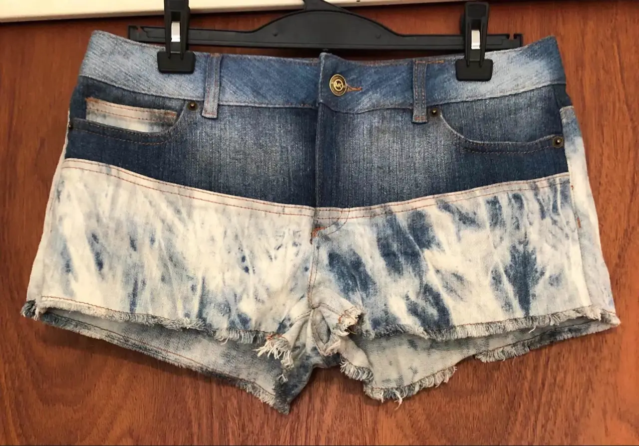 Short de jean de mujer con diseño tie dye en la parte inferior. Posee detalles de costura en color naranja y el logo de la marca Michael Kors en un botón y en la parte trasera.