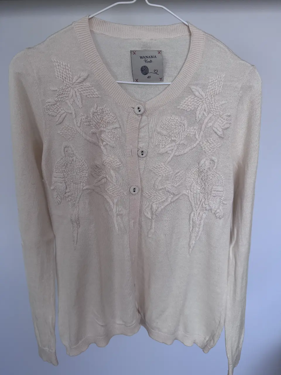 Cardigan de tejido de punto color crudo con bordado floral en relieve. Ideal para un look elegante y femenino.
