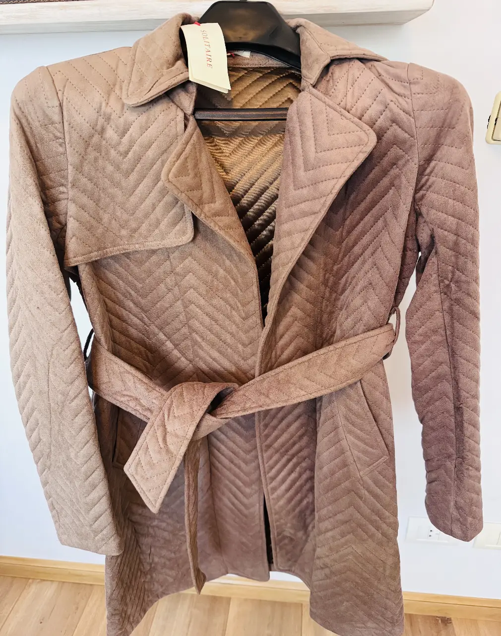 Trench de gamuza acolchado color marrón avellana. Largo total 90 cm. Posee cinturón para ajustar en la cintura y un diseño de costuras en zig-zag. Ideal para un look elegante y abrigado.