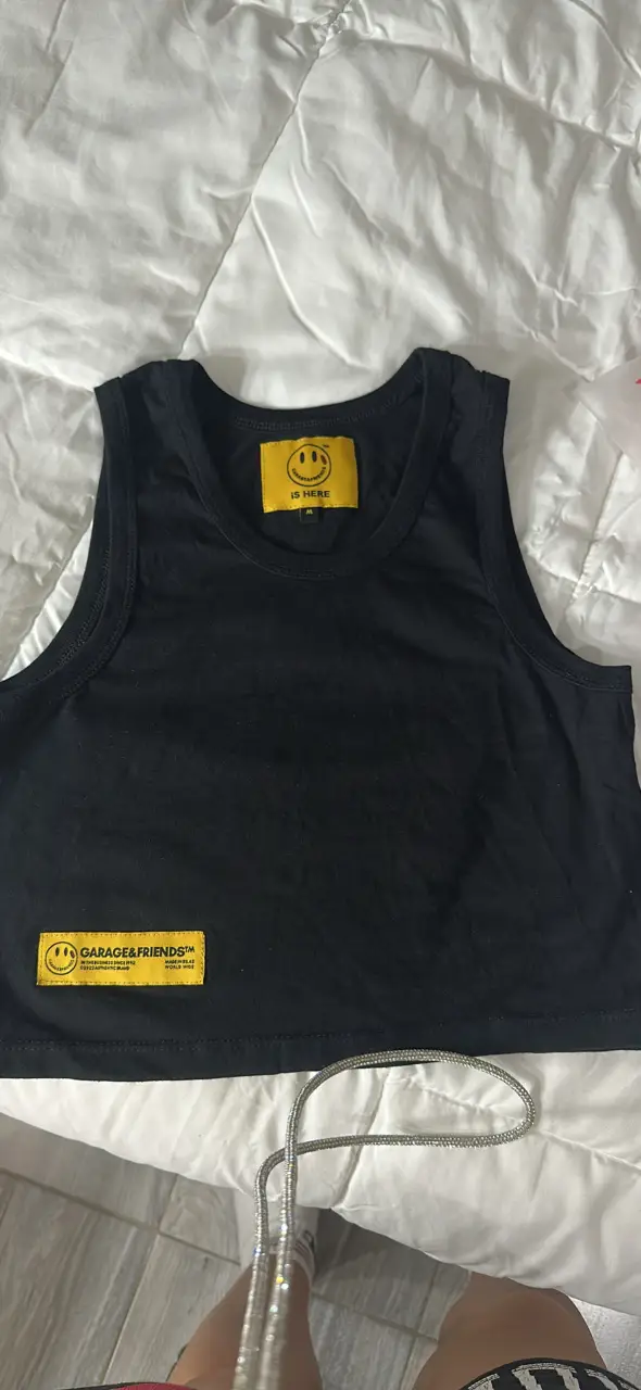 Top negro de corte crop con estampado de la marca Garage & Friends. Diseño con cuello redondo y detalle de etiqueta amarilla con el logo de la marca. Ideal para un look casual y moderno.
