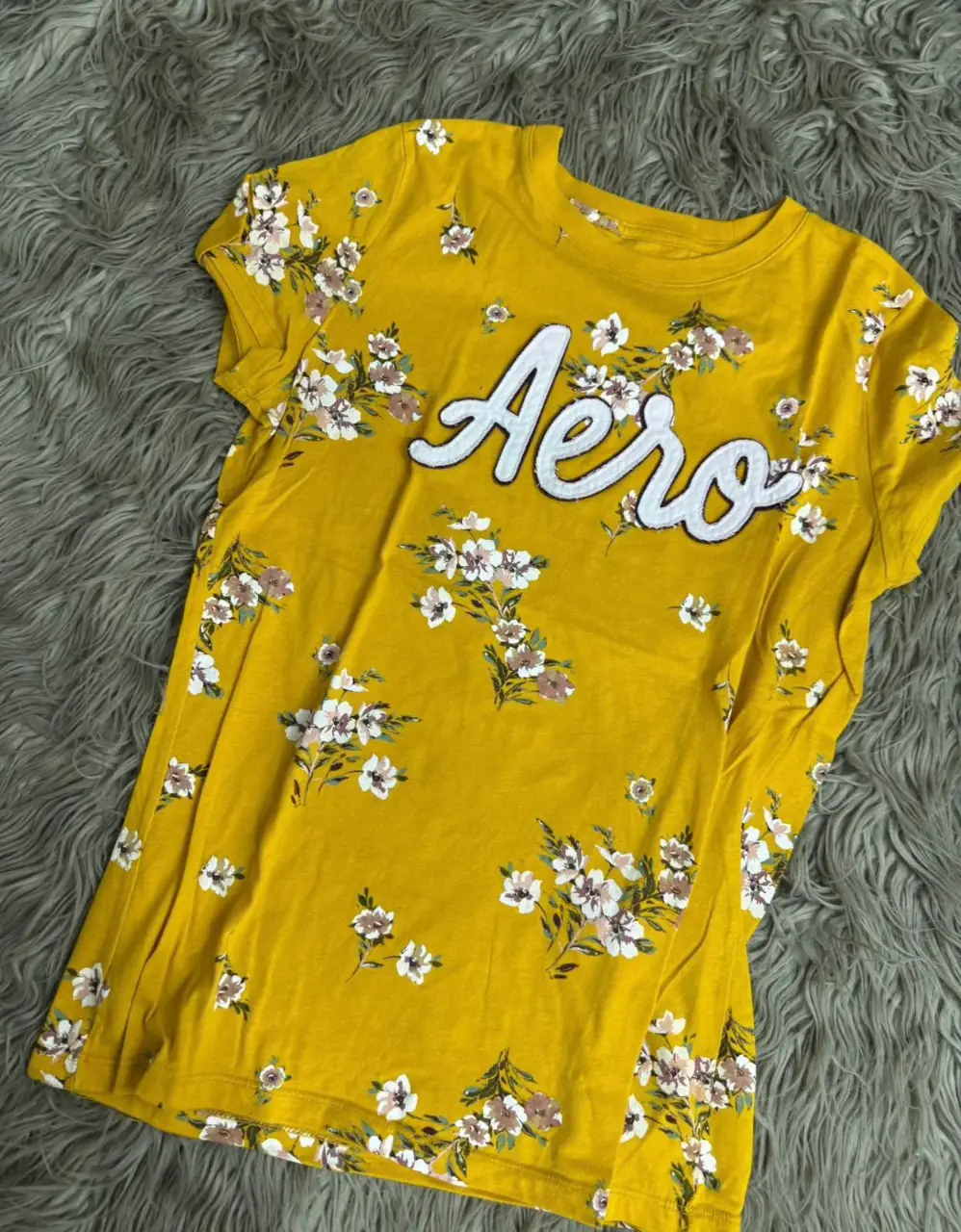 Remera Aeropostale amarilla de mujer con estampado floral y la palabra "Aero" en blanco. Ideal para un look casual y fresco.