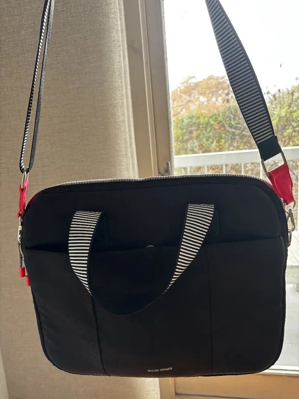 Bolso negro para llevar en el hombro, con manijas cortas y correa larga ajustable con detalles en blanco y negro. Ideal para llevar tus cosas con estilo y comodidad.