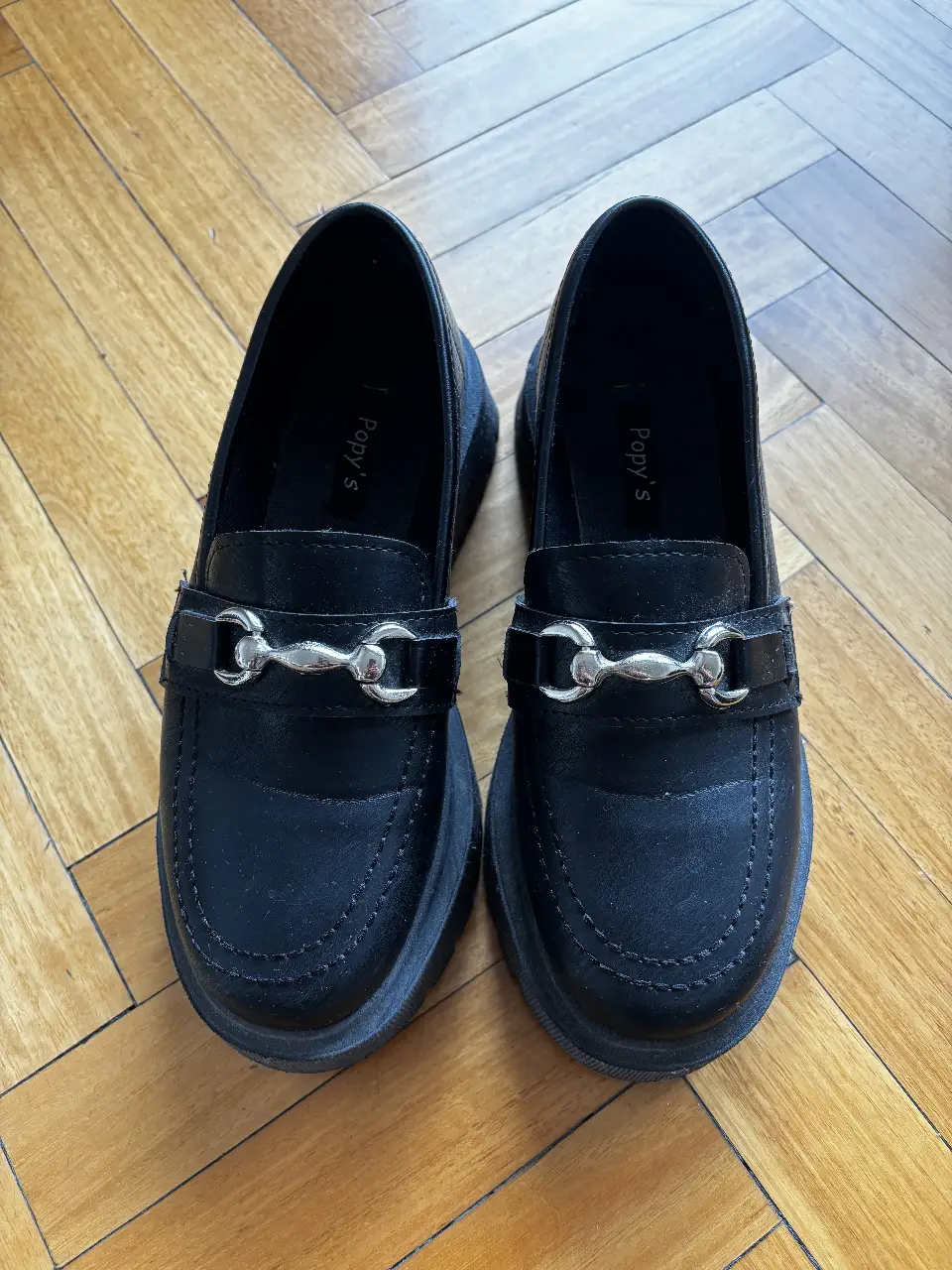 Zapatos tipo mocasín negros con suela gruesa y hebilla plateada. Ideales para un look moderno y cómodo.