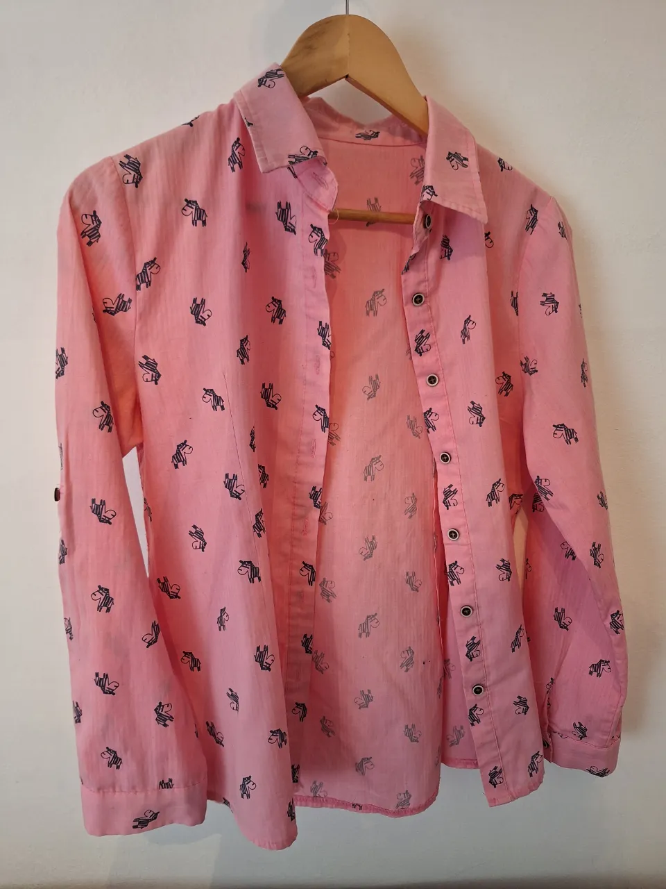 Camisa rosa con estampa de cebras en azul, cuello clásico y botones al frente. Perfecta para un look casual y divertido.