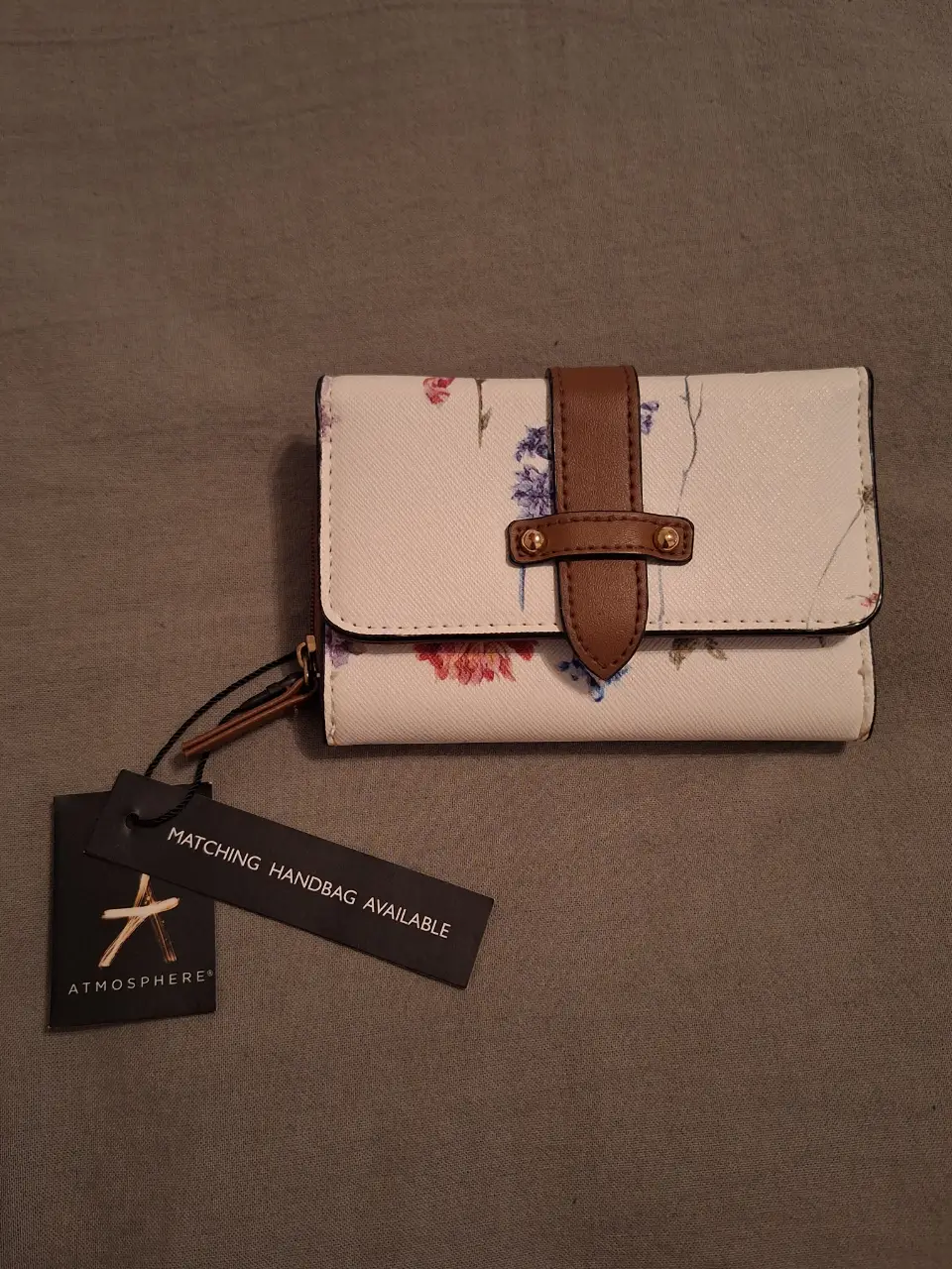 Billetera Atmosphere con estampado floral, cierre y detalle en marrón. Ideal para llevar tus esenciales con estilo.