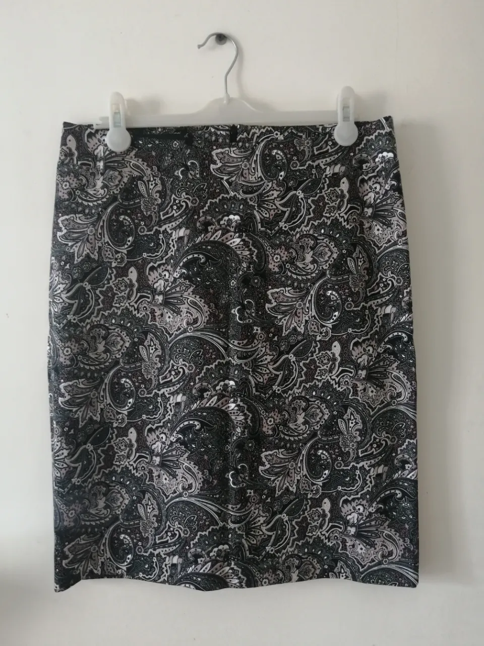 Pollera sastrera con estampado paisley en tonos grises y negros. Posee un corte clásico y elegante, ideal para el trabajo o eventos formales. Cuenta con un detalle de abertura en la parte inferior trasera para mayor comodidad.