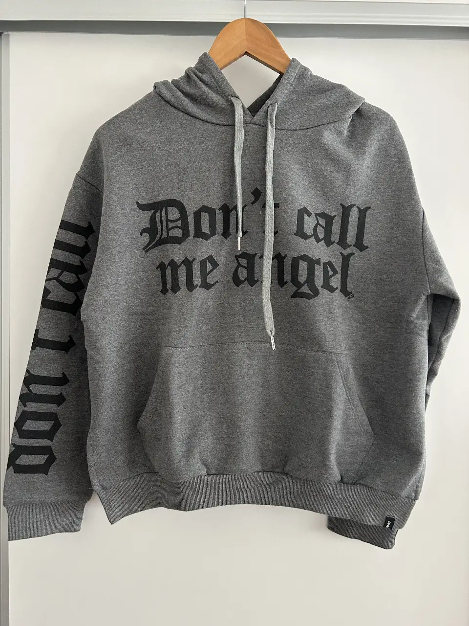 Buzo canguro gris con capucha y estampado "Don't call me angel" en negro. Estilo streetwear, ideal para un look casual y cómodo.