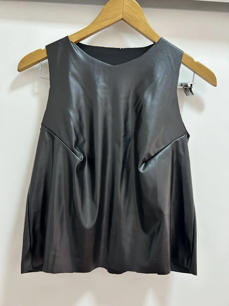 Top negro de cuero sintético, sin mangas, con diseño drapeado y corte asimétrico. Ideal para un look moderno y audaz.
