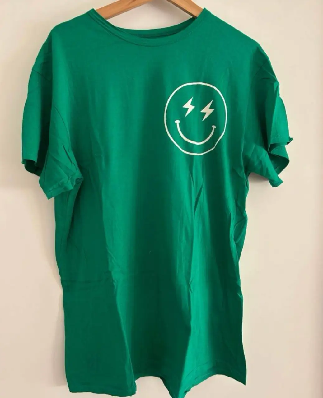 Remera verde con estampado de sonrisa y rayos en el frente y frase "IT'S A GOOD DAY TO HAVE A GOOD DAY" en la espalda. Ideal para un look casual y relajado.