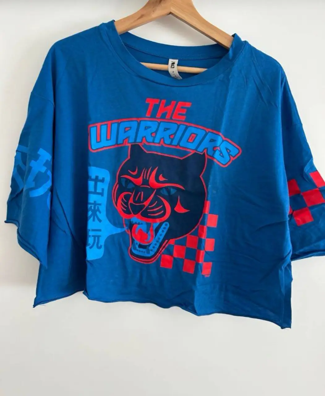 Remera de hombre azul con estampado de "The Warriors". Corte crop, manga 3/4. Estilo retro y deportivo.