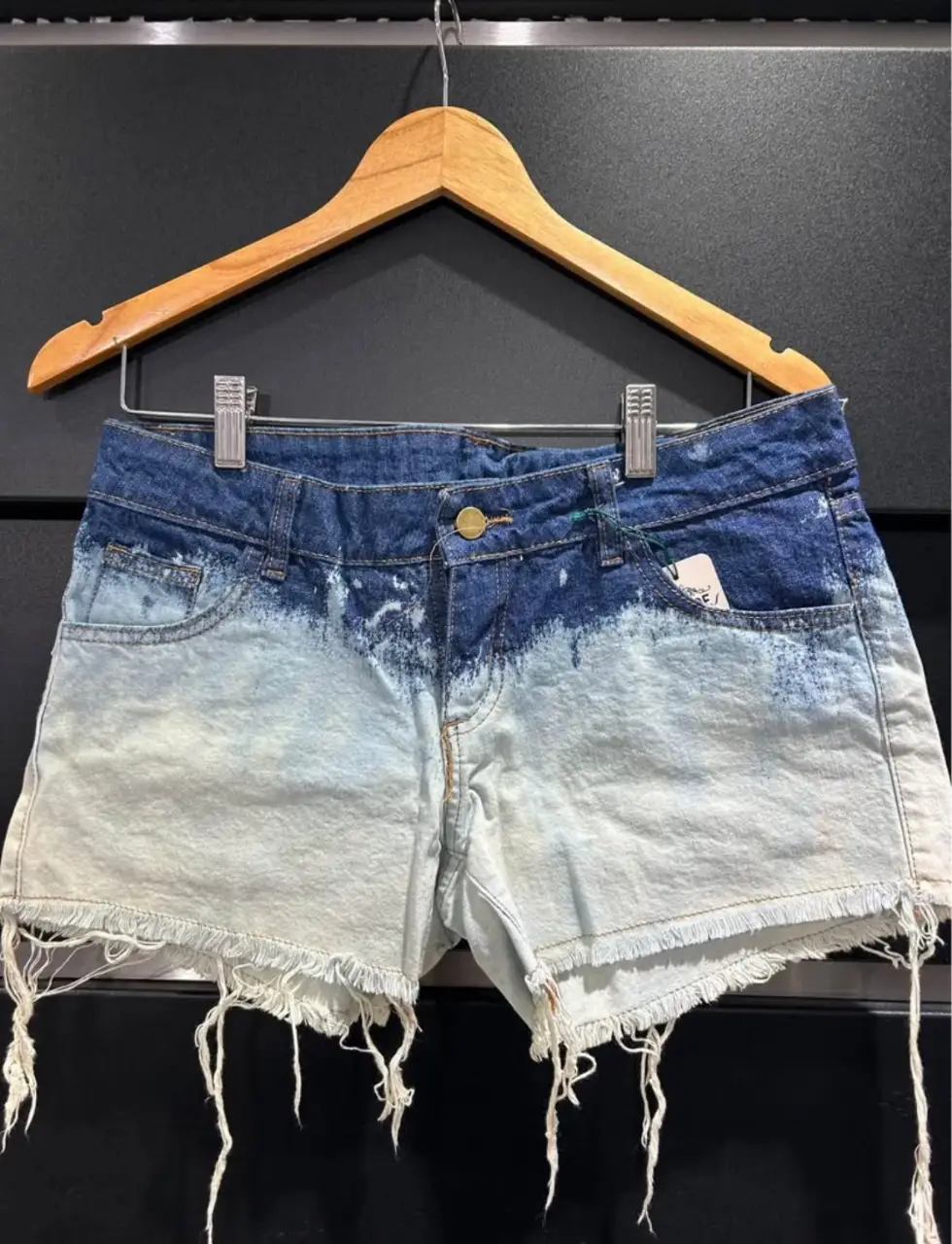 Short de jean de mujer con efecto degradado. Tiro medio/bajo, con detalles de desgaste en los bordes y flecos. Ideal para un look casual y moderno.