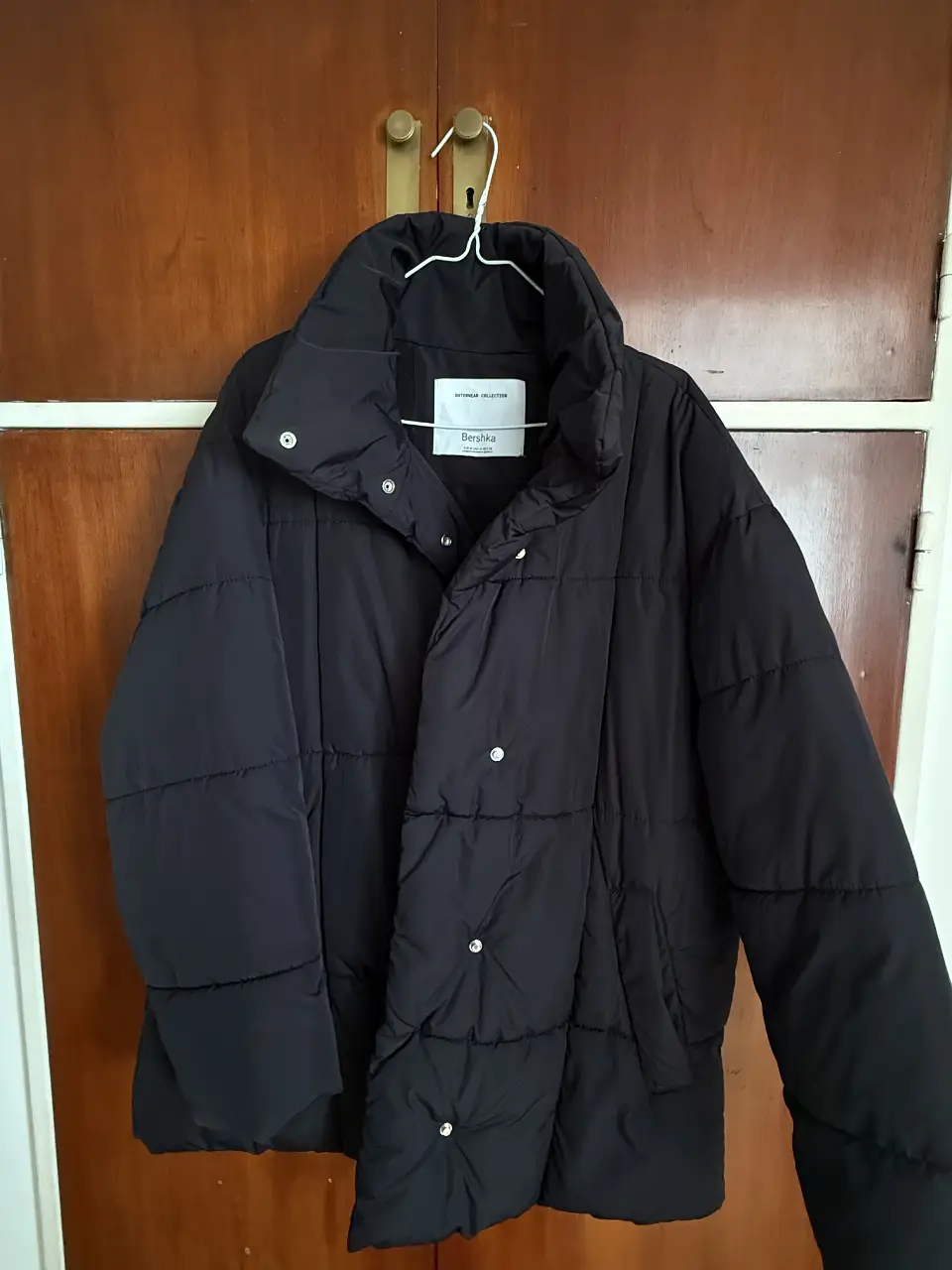 Campera puffer negra oversize de la marca Bershka, ideal para el invierno. Confeccionada con materiales resistentes y diseño acolchado, ofrece abrigo y estilo. Tiene cierre con botones y cuello alto.