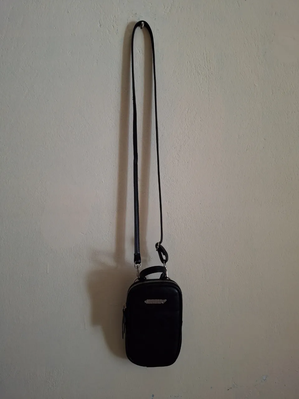 Cartera negra porta celular  de cuero sintético, marca Scombro con diseño acolchado y detalles plateados. tiene un cierre dentro y esta forrado en tela con estampado en negro ,  Ideal para llevar lo esencial con estilo. 
medidas.. 
alto 
ancho
profundidad