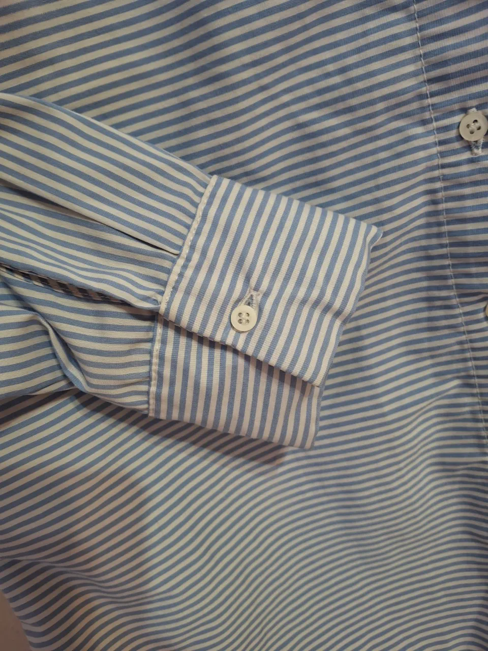 Camisa a rayas celestes y blancas, manga larga con puño y botón. Posee un bolsillo en el frente y cuello clásico. Ideal para un look casual o para ir a trabajar.