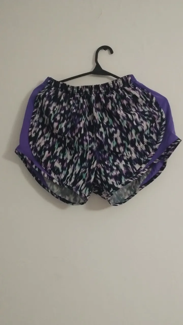 Short deportivo de mujer, con estampado abstracto en tonos violetas, negros y blancos. Detalles en violeta liso en los laterales. Ideal para running y entrenamientos.