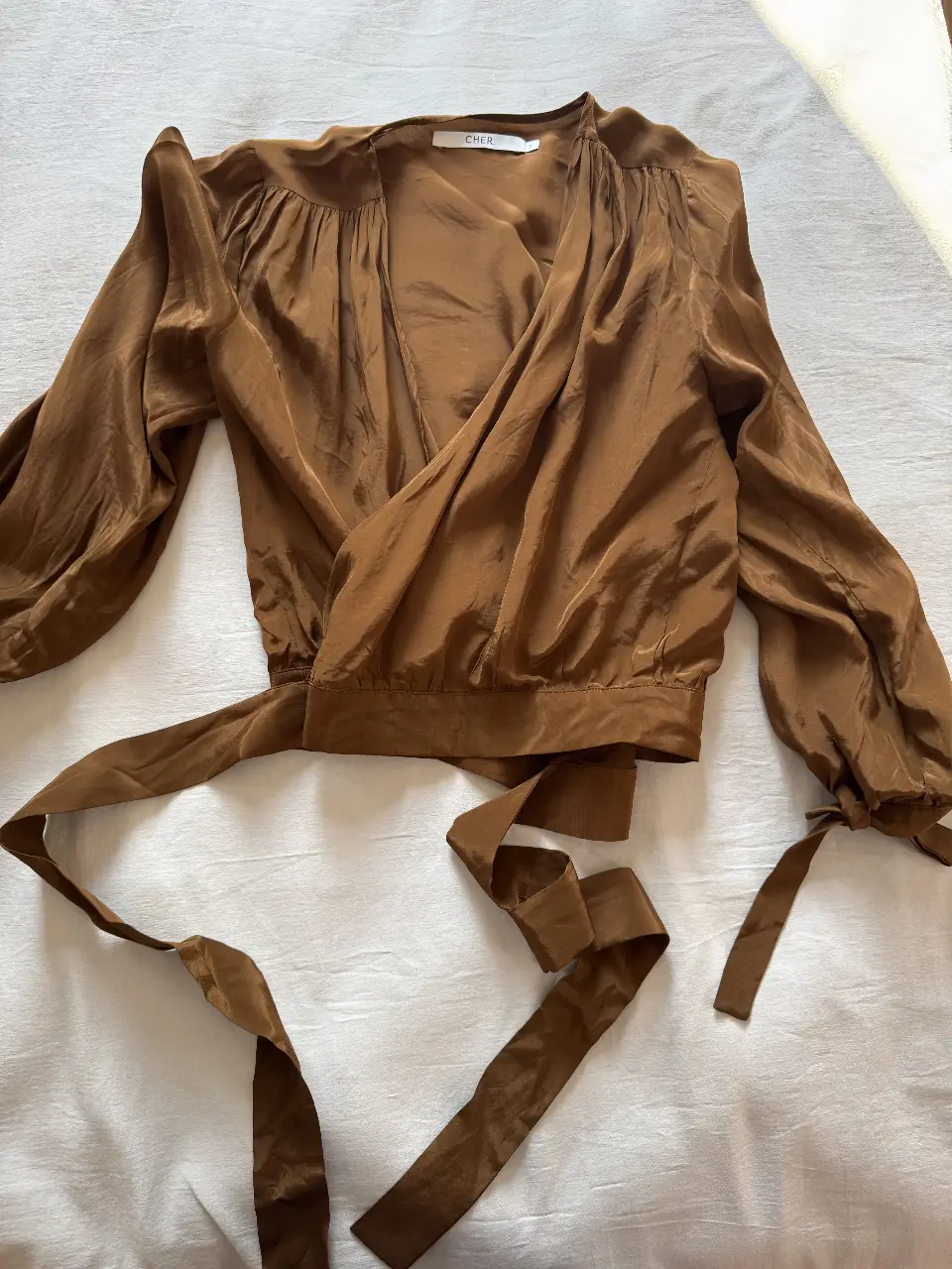 Blusa marrón MARÍA CHER de SÍMIL seda con mangas largas abullonadas y detalle cruzado. Ideal para un look elegante y sofisticado.
