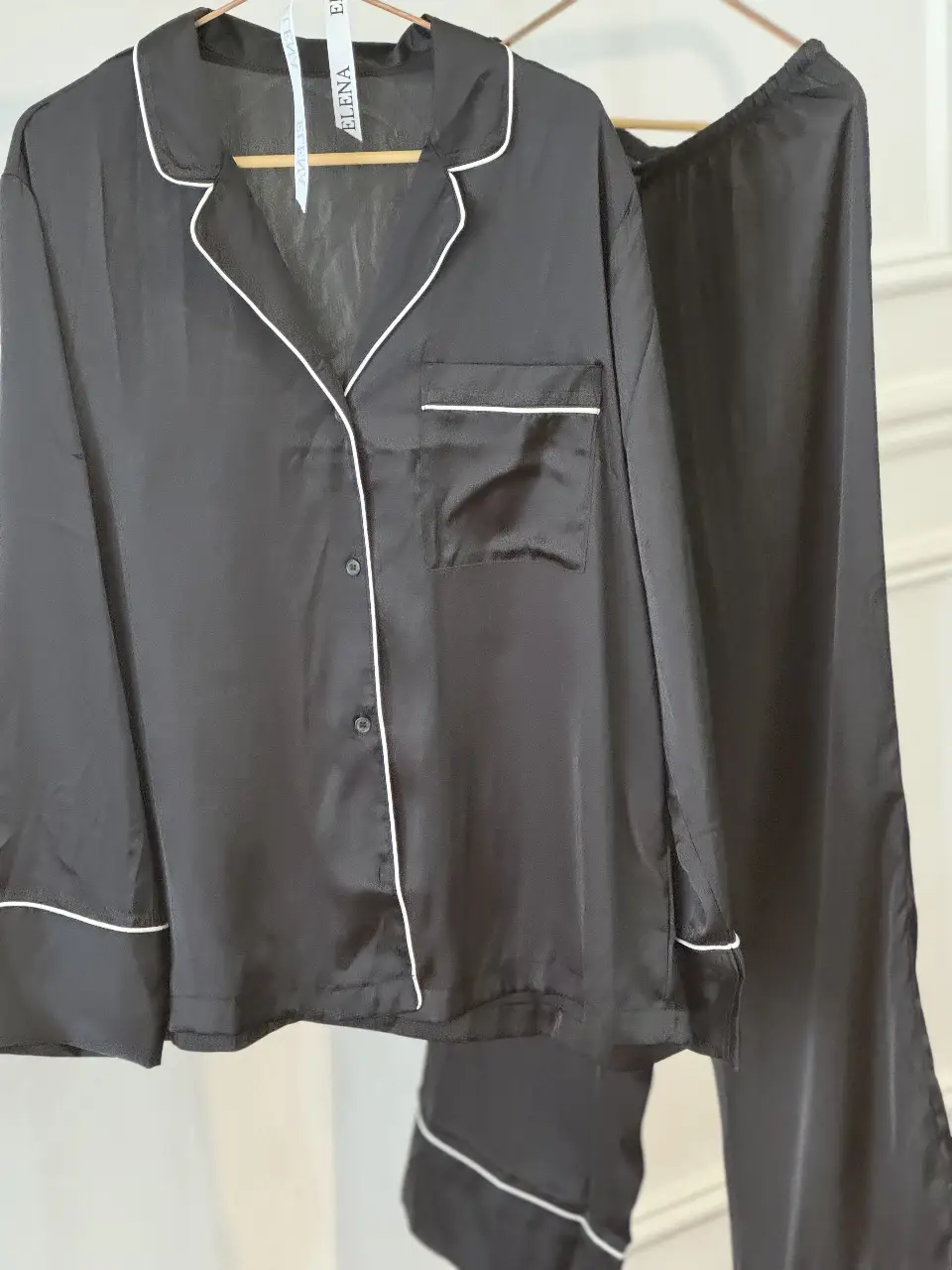 Conjunto de pijama de satén negro con detalles en blanco. Camisa con botones y bolsillo en el pecho, pantalón con terminación en blanco. Ideal para un descanso cómodo y elegante.