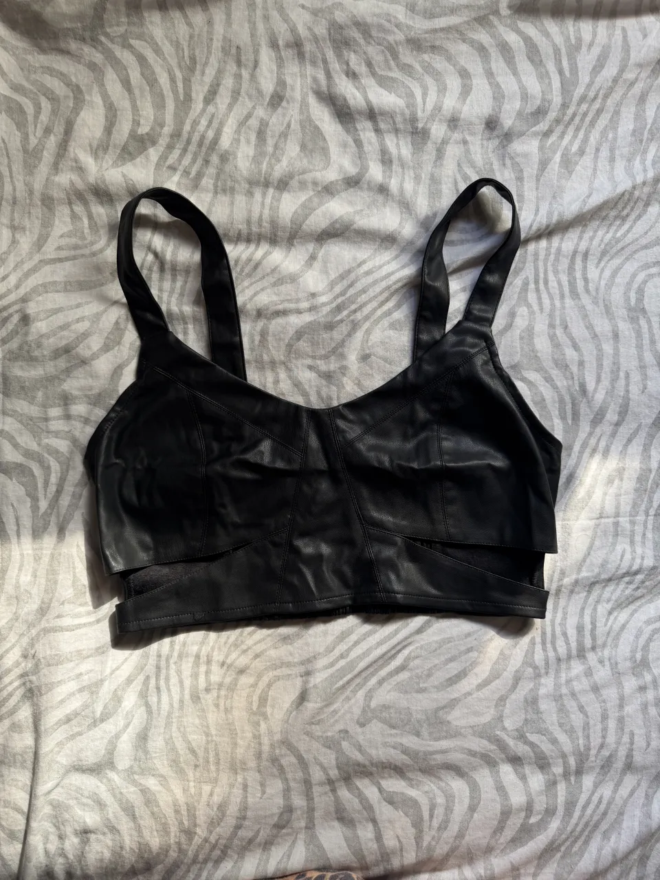 Top negro de cuero sintético con detalles de tiras y fruncido en la cintura. Ideal para un look audaz y moderno.