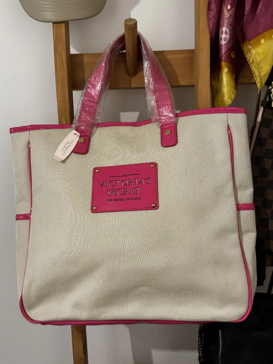 Bolso tote de Victoria's Secret en color blanco con detalles en rosa. Cuenta con un aplique rectangular con el logo de la marca. Ideal para llevar tus esenciales con estilo.