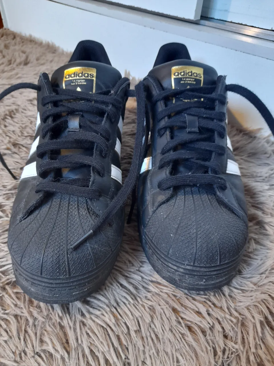 Zapatillas Adidas Superstar negras con detalles blancos y dorados. Cierre de cordones.