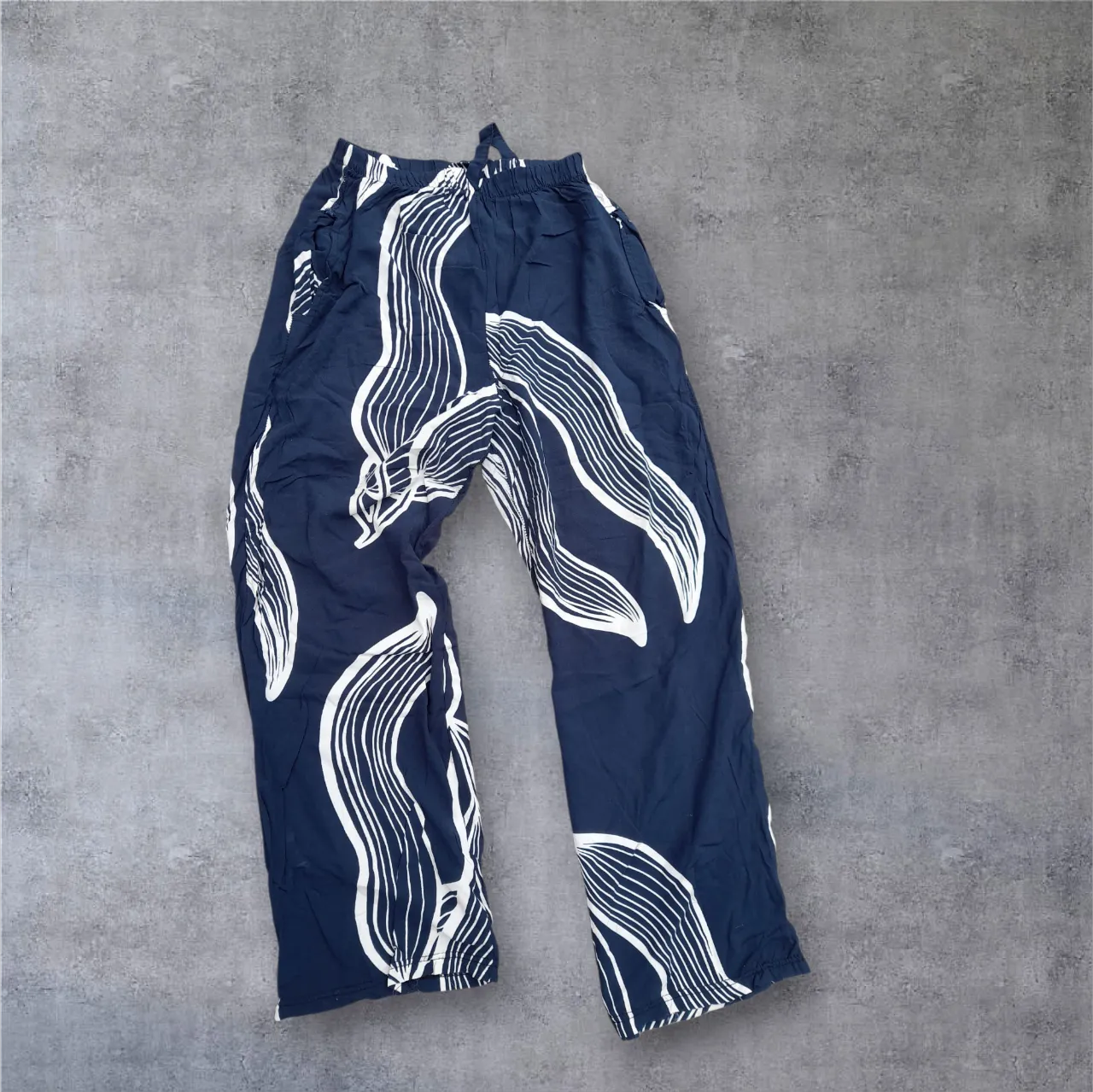 Pantalón de tela azul marino con estampado abstracto blanco. Diseño suelto y cómodo, ideal para un look relajado y canchero. Cintura elastizada con cordón.

👕 Pantalón azul y blanco 
🧵 Material: 100% algodón 
📏 Medidas: talle 2 . Cintura 30/43cm. Cadera 56cm.tiro delantero 32cm. Largo total 94cm. 
