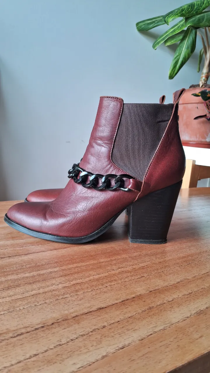 Botitas de cuero color marrón con cadena negra decorativa. Taco grueso y elástico lateral para facilitar el calce. Ideales para un look canchero y moderno. Marca Uma.