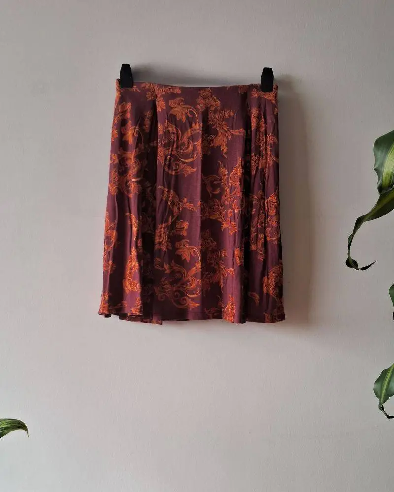 Pollera Uma color bordó con estampa naranja. Elástico en cintura. Talle S (38). Medidas aproximadas: cintura 30cms, largo 45cms. Posee dos pliegues, tiene algo de vuelo (no es tubo). Composición: 95% viscosa, 5% elastano.