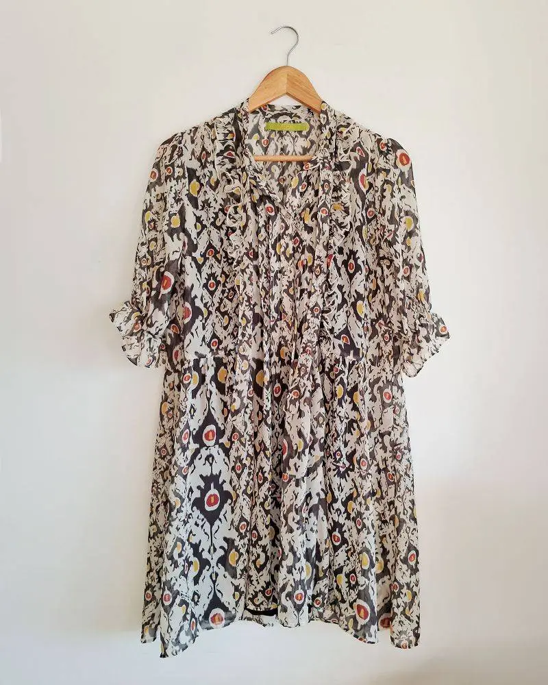 Vestido Rapsodia de corte amplio, tela tipo gasa semitransparente. Volados en el frente, con pinzas verticales. Tres botones frontales, lazo en el cuello, mangas 3/4 con terminación elástica y volados. La etiqueta del talle está cortadas. Medidas aprox: hombros 36cm, e/sisas 50cm, largo 86cm