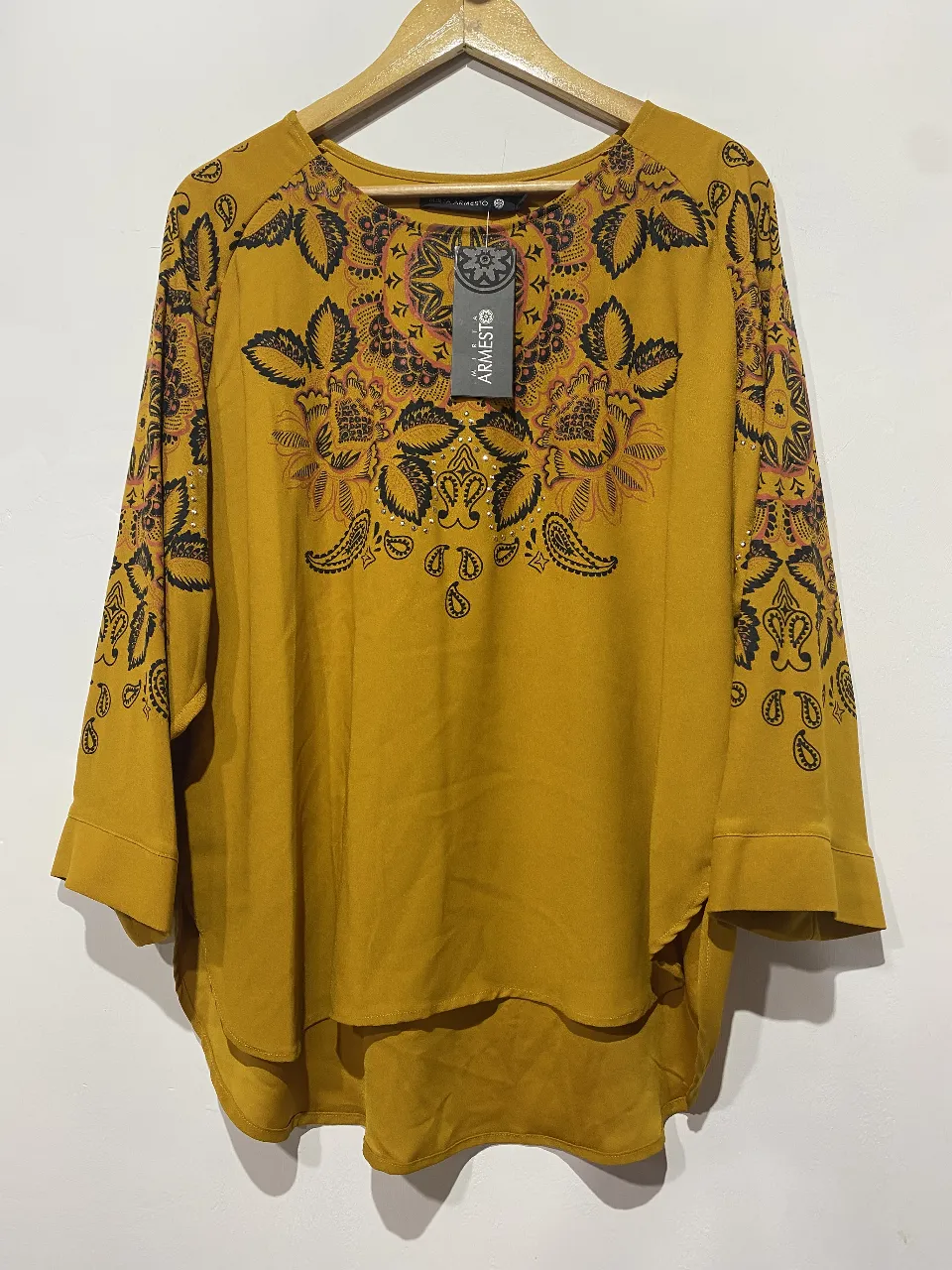 Blusa de seda color mostaza con estampa floral y paisleys en negro y detalles en coral. Posee mangas 3/4 y un corte asimétrico moderno. Ideal para un look canchero y con onda.