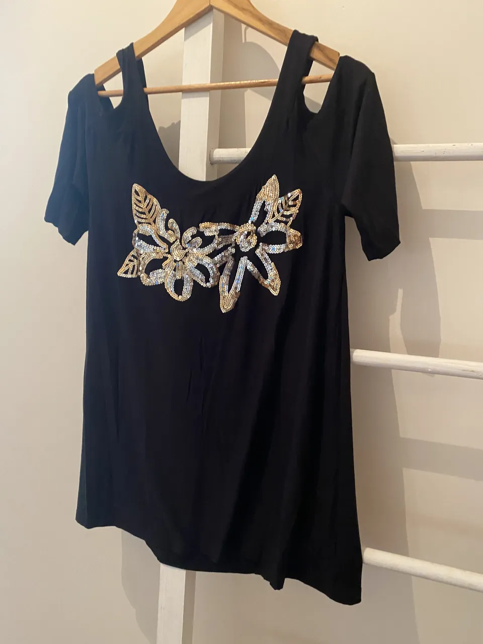 Remera negra con detalles de lentejuelas doradas y plateadas en forma de flores. Tiene un escote pronunciado y tiras finas en los hombros que dejan la parte superior al descubierto. Ideal para un look canchero y con un toque de brillo.