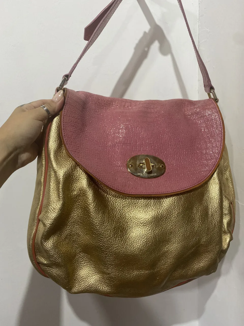 Bolso de cuero dorado con solapa texturizada en rosa. Cierre metálico y correa regulable. ¡Un accesorio que no pasa desapercibido!