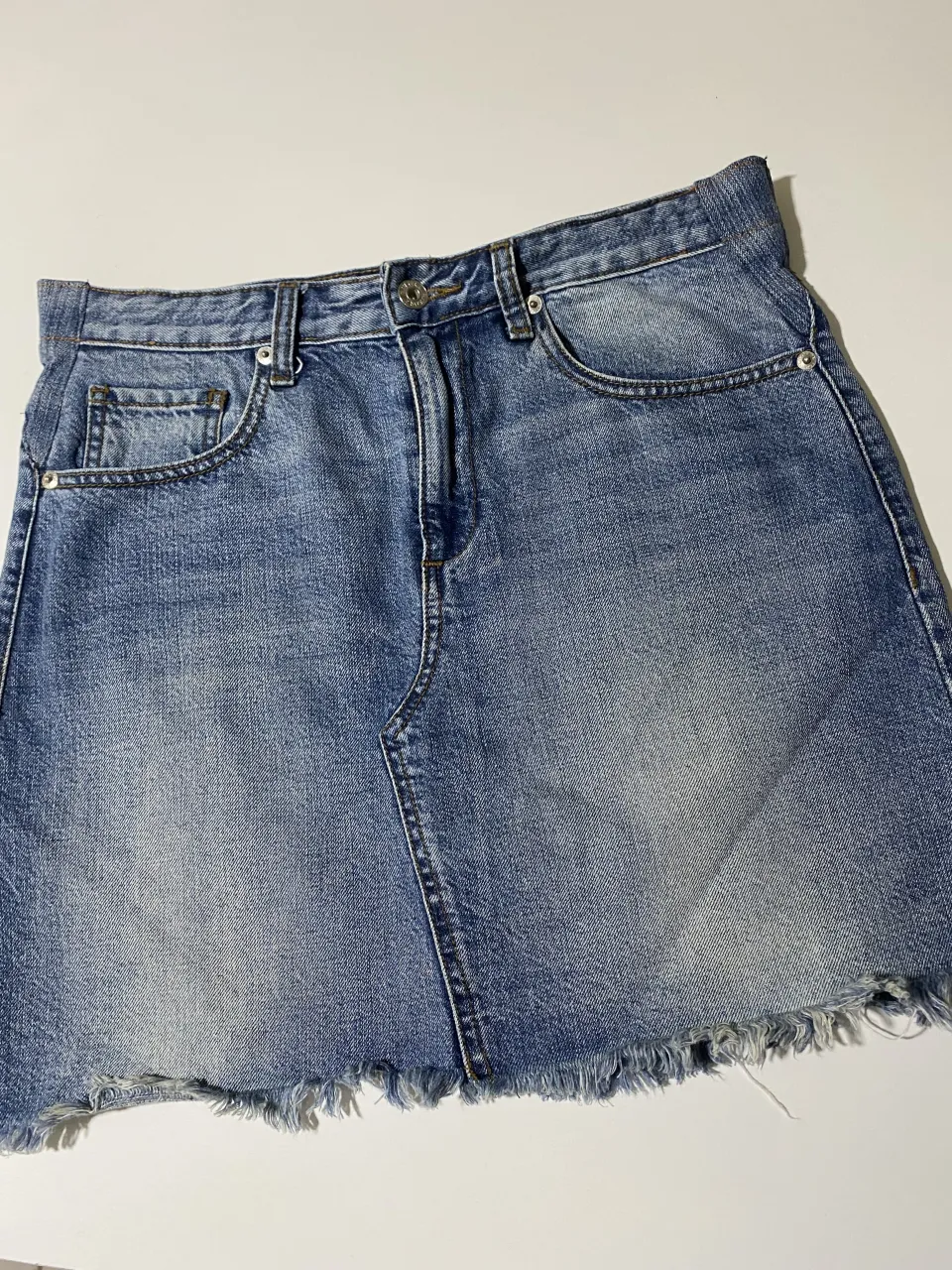 Pollera de jean azul con roturas y flecos en el ruedo. Tiene parches de jean en la parte trasera.