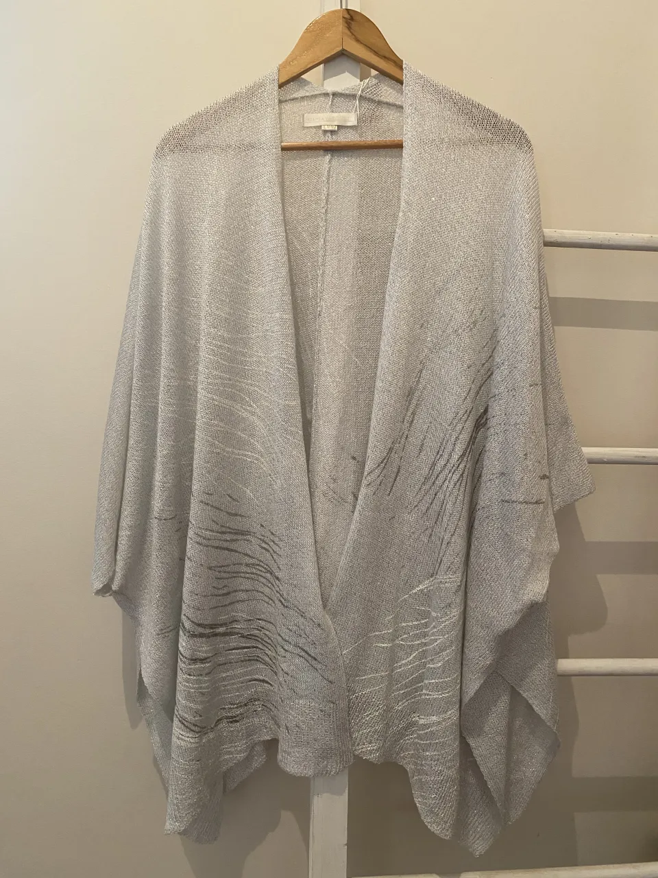 Cardigan tejido plateado con detalles de líneas plateadas y roturas sutiles. Diseño abierto y liviano, ideal para complementar cualquier look.