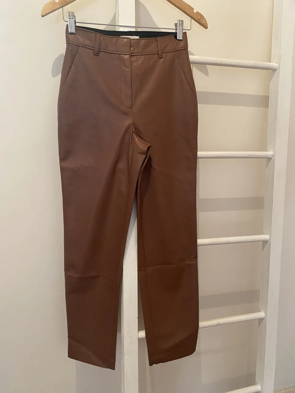Pantalón de cuero marrón, tiro alto, corte recto y largo hasta el tobillo. Un básico súper canchero para elevar cualquier look. Ideal para usar con botas o zapatillas.