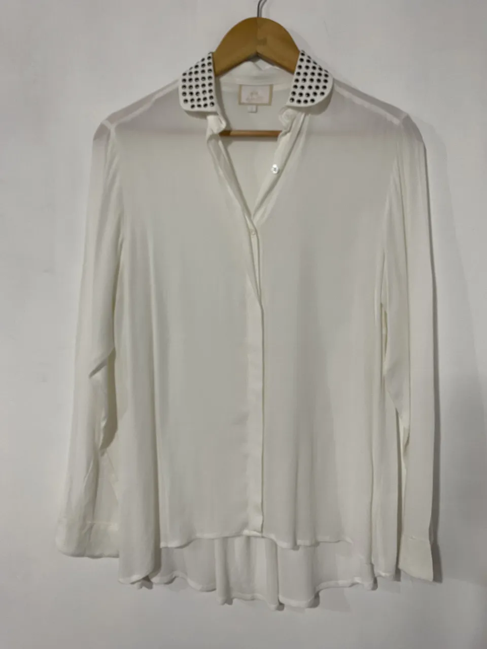 Camisa blanca de seda con cuello estilo Peter Pan adornado con tachas negras. Posee botones al tono y un corte moderno.