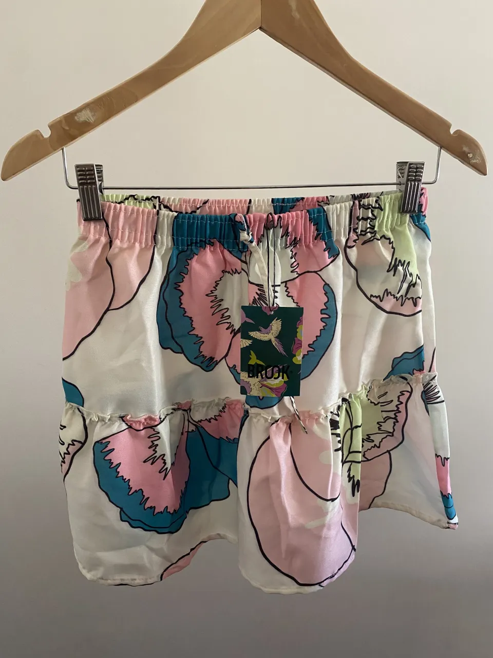 Shorts blancos con estampado floral grande en tonos rosa, azul y verde. Cintura elastizada con cordón y volados en la parte inferior.