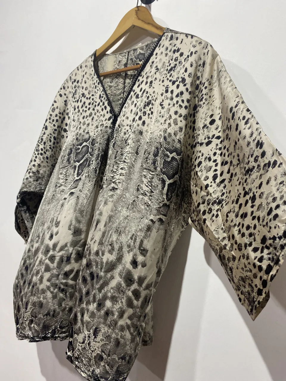 Blusa estampada con diseño animal print y detalles de serpiente. Posee un cierre metálico con strass en el frente y mangas amplias tipo murciélago. Ideal para un look audaz y moderno.