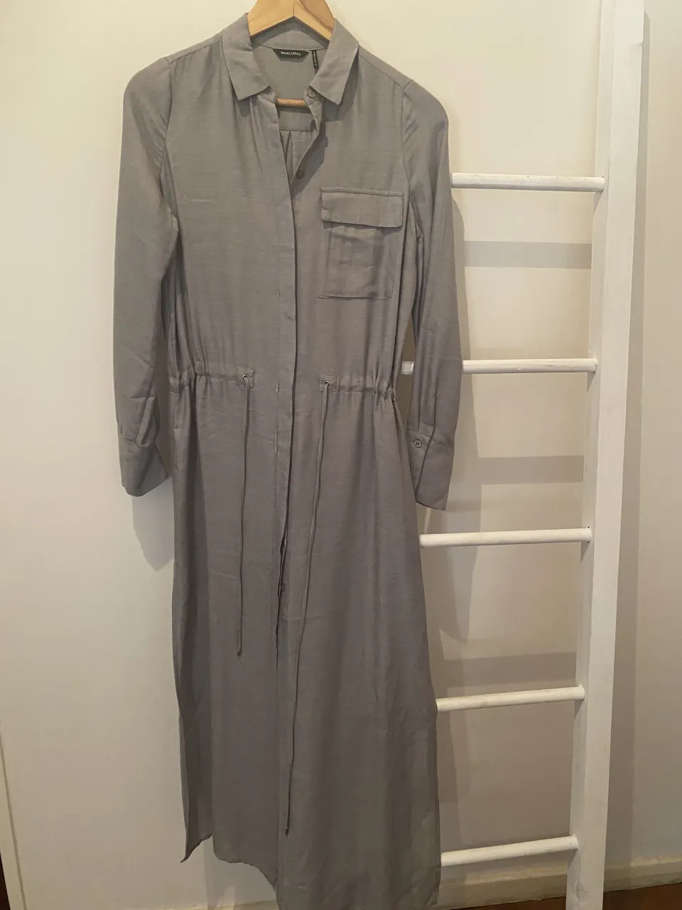 Vestido camisero largo gris, con cinturón de ajuste en la cintura y bolsillos frontales. Ideal para un look casual y elegante.