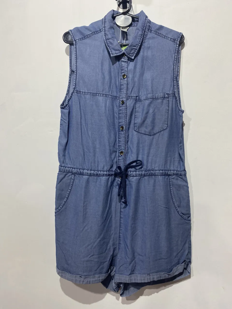 Mono de jean sin mangas, con cuello camisero, botones al frente, cintura ajustable con cordón y bolsillos laterales. Ideal para un look casual y canchero.