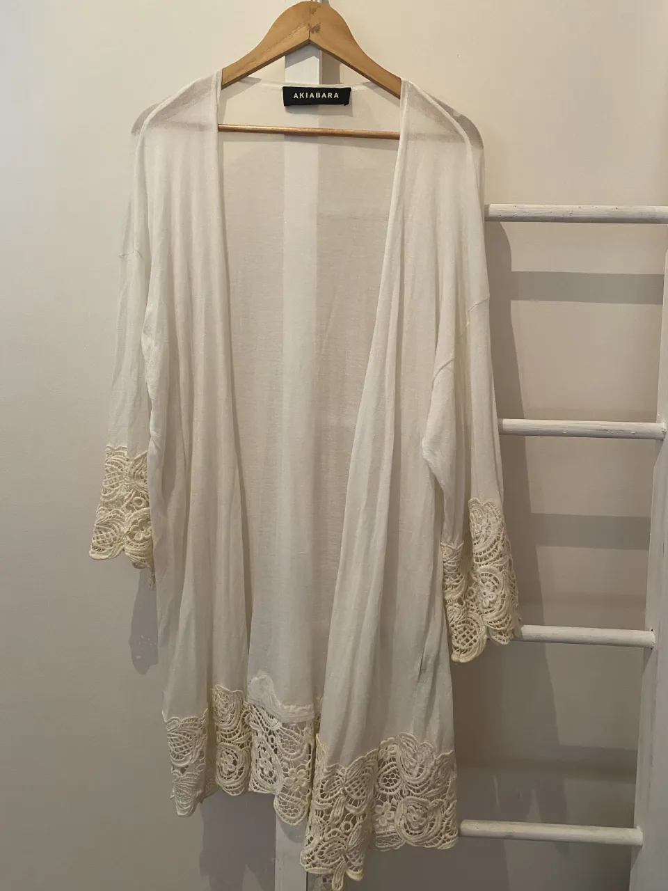 Cardigan largo de hilo blanco con detalles de encaje en mangas y ruedo. Ideal para usar sobre bikinis o como accesorio de moda en días de playa o salidas casuales. Su diseño liviano y vaporoso lo hace perfecto para el verano.