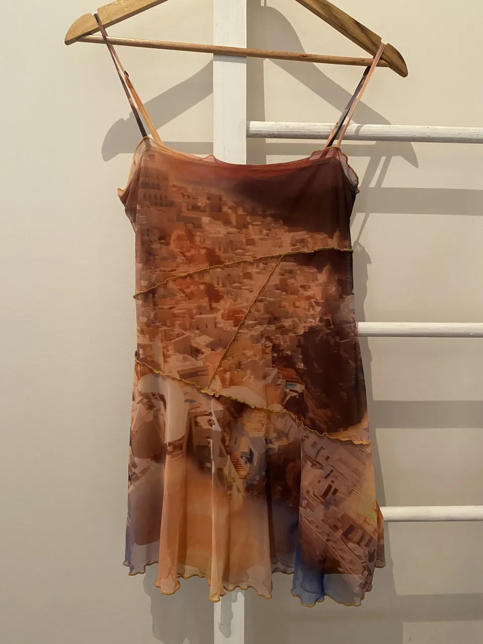 Vestido corto con estampa de paisaje urbano, ideal para un look veraniego y canchero. Su diseño con tiras finas y detalles de volados en el ruedo le da un toque femenino y moderno. Perfecto para combinar con sandalias o zapatillas.