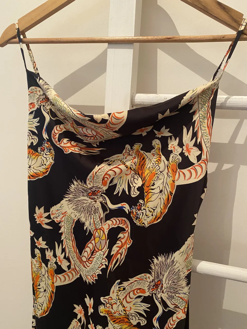 Vestido corto con estampado de dragones y tigres en tonos vibrantes sobre fondo negro. Diseño con tirantes finos y escote drapeado, ideal para un look audaz y llamativo.